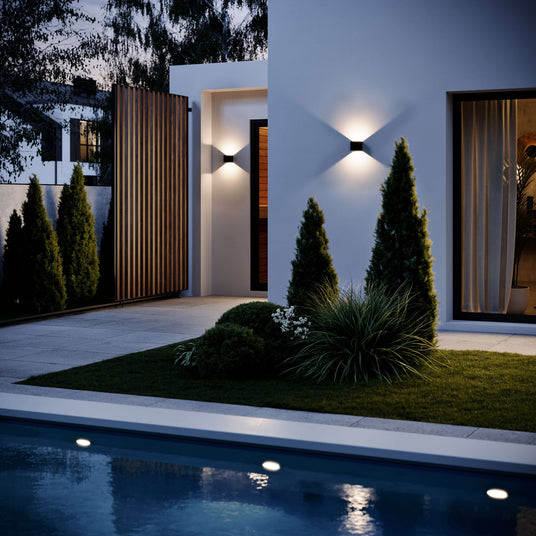 Elegante Außenbeleuchtung am modernen Haus mit Hecken, Rasen und Pool im nächtlichen Ambiente.