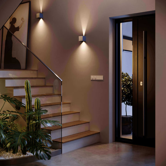 Moderne Treppe mit Pflanzen und eleganter Eingangstür, beleuchtet von stilvollen Wandleuchten.