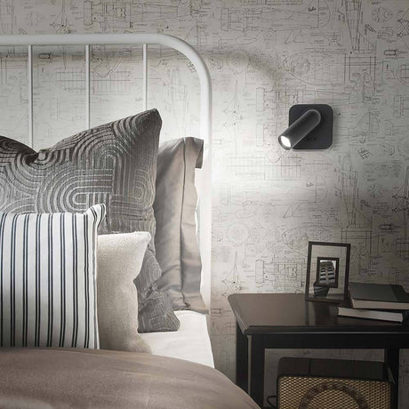 Bean Square LED Wandstrahler neben einem Bett mit dekorativen Kissen und einem Nachttisch.