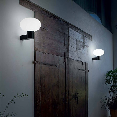 Clio Außen-Wandlampe IP44 an einer rustikalen Holzwand installiert, sanftes Licht verbreitend.