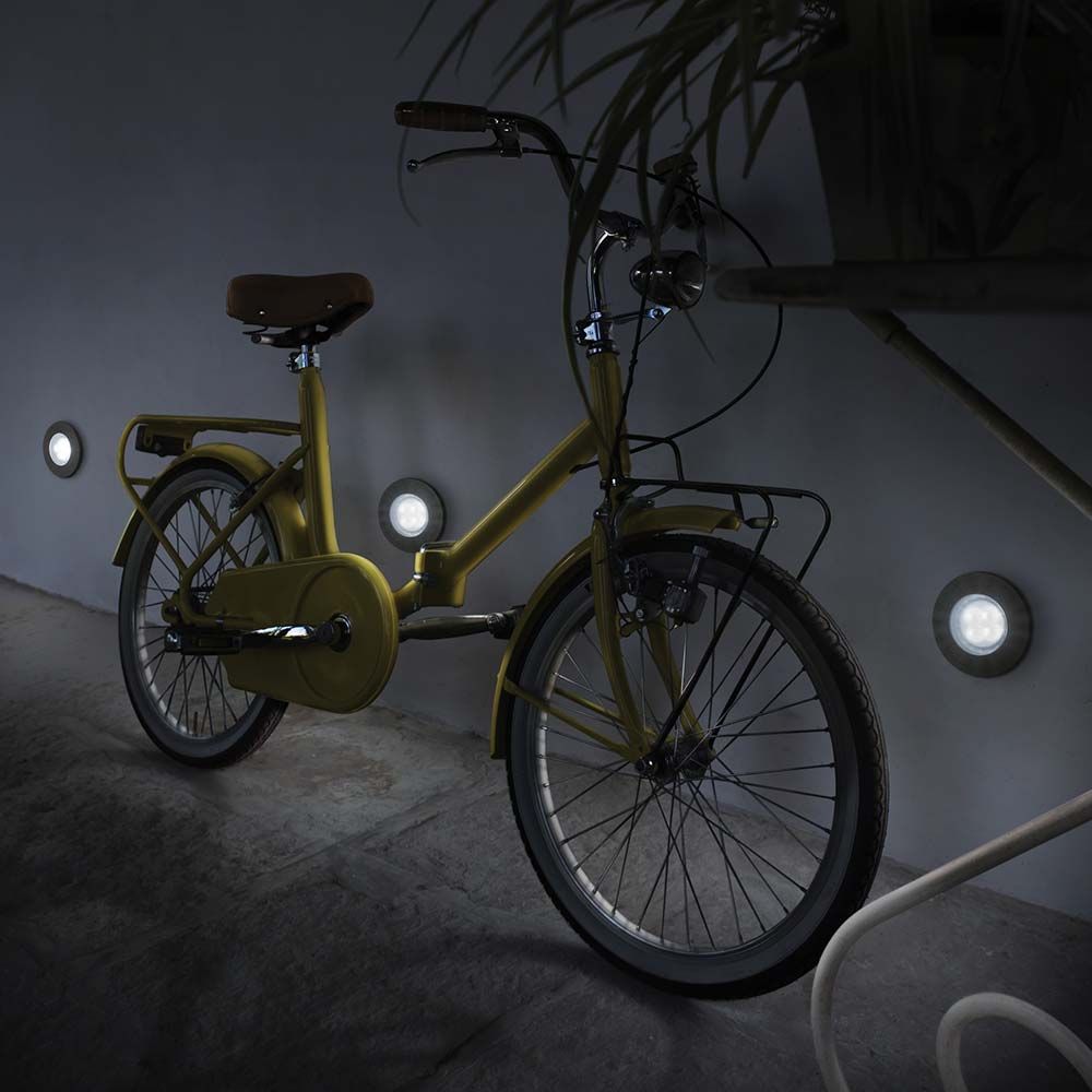 Ein gelbes Fahrrad im Dunkeln, neben leuchtenden Wandstrahlern, die für eine stilvolle Beleuchtung sorgen.