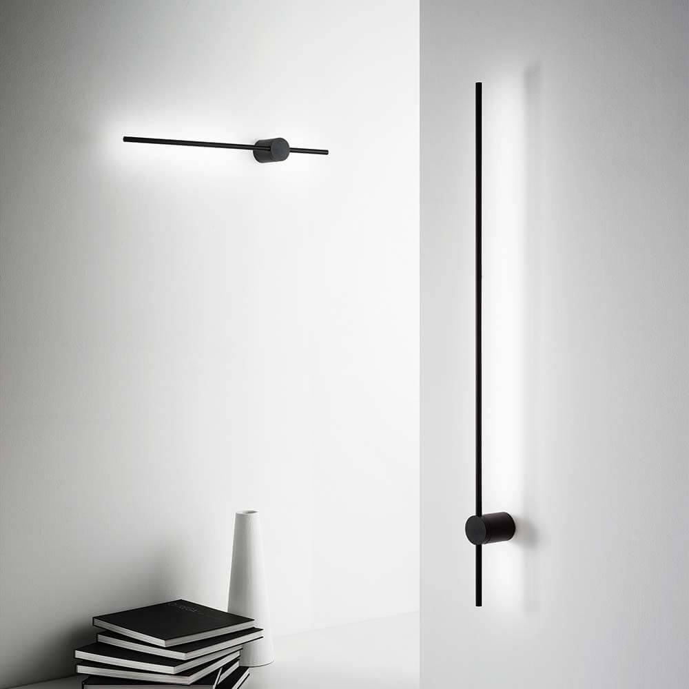 Essence LED Wandleuchte in modernem Design, im Hintergrund schwarz-weißer Raum mit minimalistischer Dekoration.