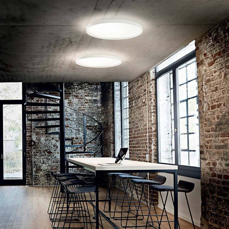 Moderne Raumansicht mit Fly LED Deckenleuchte Weiß über einem Tisch und industriellem Hintergrund.