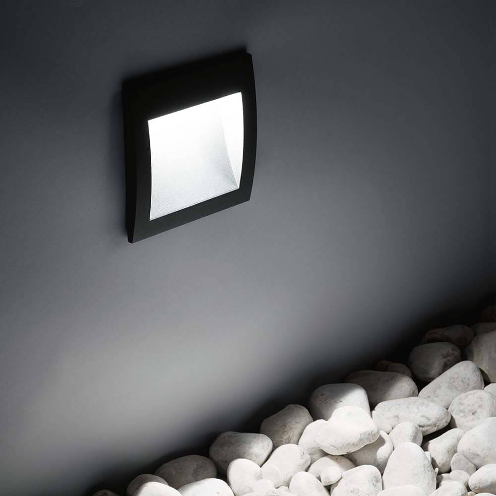 LED Außen Wandleuchte IP65 an einer Wand über weißen Kiessteinen montiert.