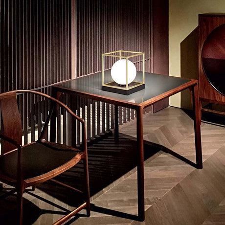 Lingotto bordlampe guld på et bord i et moderne rum med en stol.