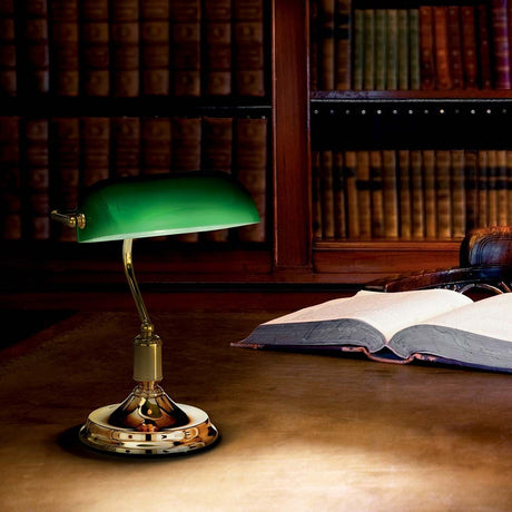Skrivebordslampe Lawyer Tl1 Ottone på et skrivebord med en åpen bok og en bokhylle i bakgrunnen.