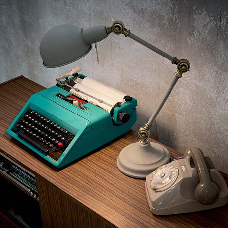 Tischleuchte Truman Tl1 Grau auf einem Holztisch mit einer alten Schreibmaschine und einem Vintage-Telefon.