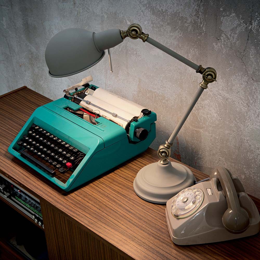 Tischleuchte Truman Tl1 Grau auf einem Holztisch mit einer alten Schreibmaschine und einem Vintage-Telefon.