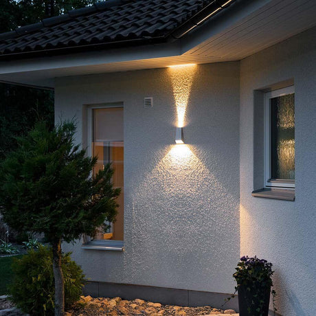 Imola LED Lampada da parete esterna con doppio cono di luce grigia su una parete di casa al buio.