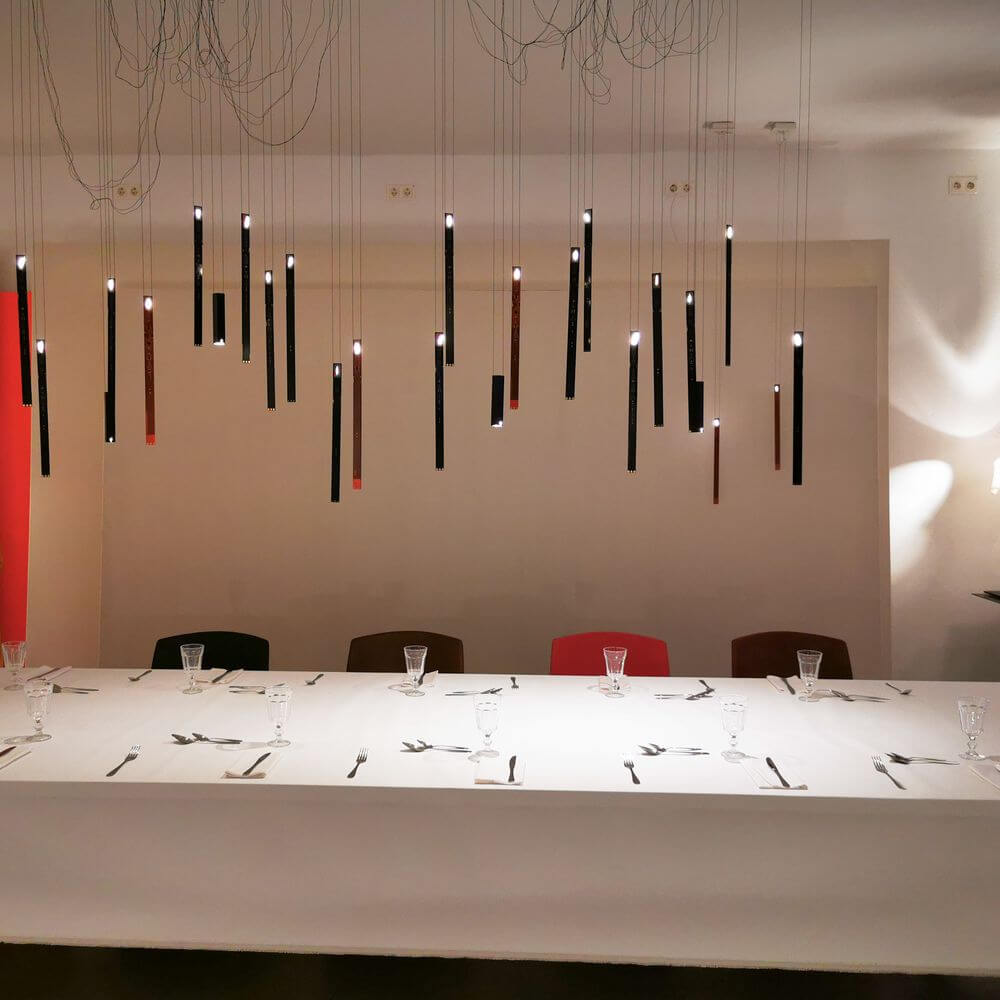 Elegante Beleuchtung mit hängenden Downlights über einem festlich gedeckten Tisch in modernem Ambiente.