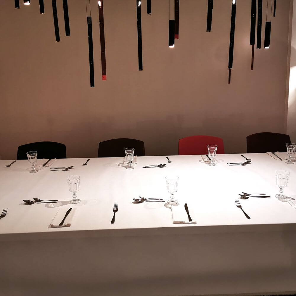 Elegant gedeckter Tisch mit Besteck und Gläsern, unter moderner Beleuchtung mit hängenden Leuchten.