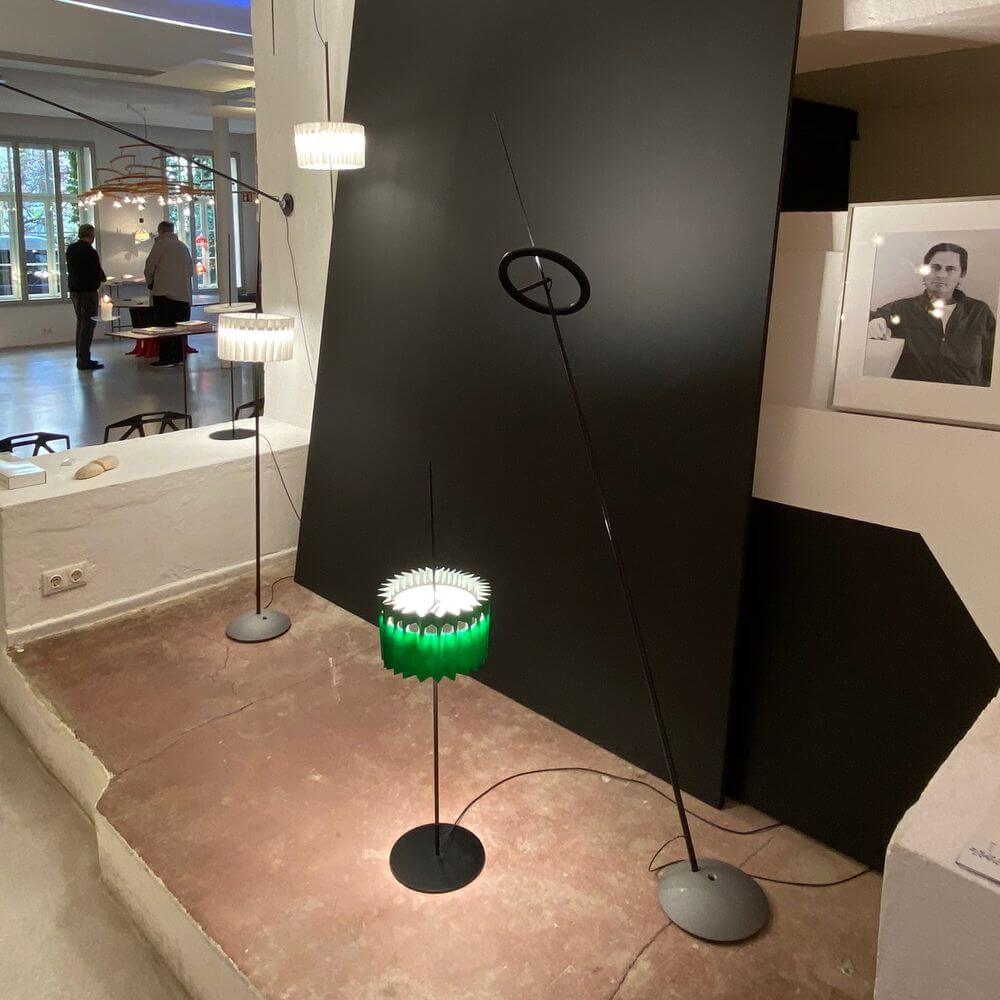 Ingo Maurer LED Stehleuchte Ringelpiez mit drehbarem Ring vor modernem Hintergrund in einem Ausstellungsraum.