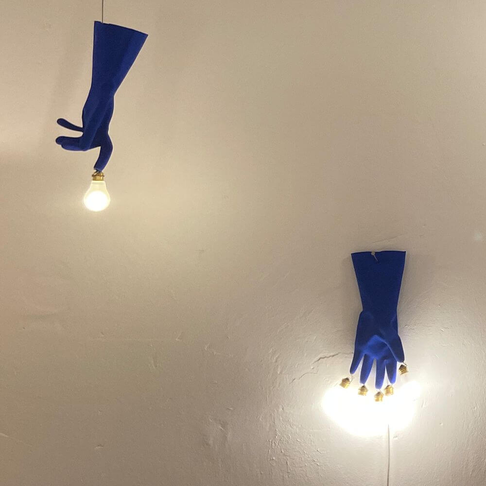 Ingo Maurer LED Wandlampe Luzy On The Wall Gummihandschuh blau an der Wand montiert mit Glühbirne.