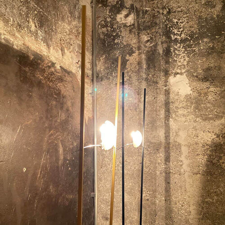 Ingo Maurer Stehlampe Ilios Designklassiker mit Opalglas und langen Metallstäben vor rauer Wand