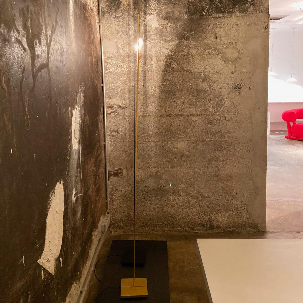 Ingo Maurer Stehlampe Ilios Designklassiker in minimalistischer Umgebung mit grauer Wand.