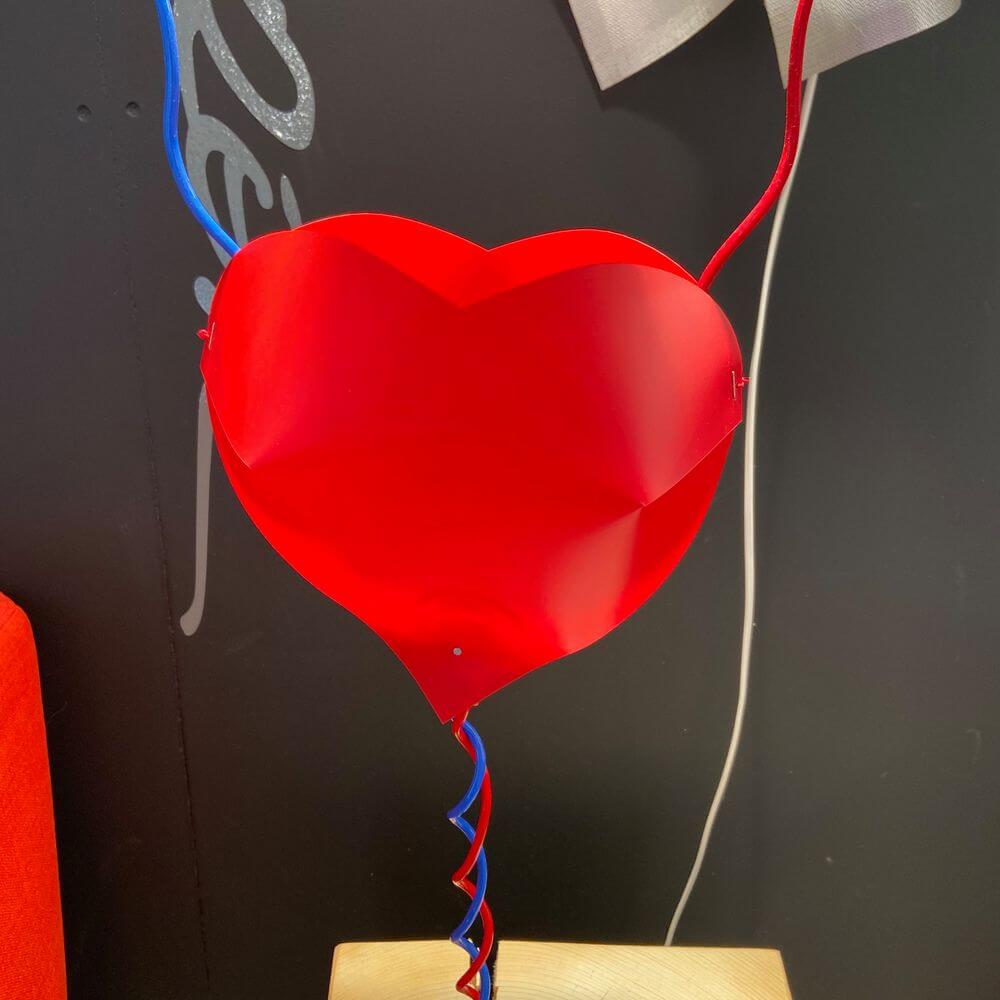 Ingo Maurer LED Tischlampe One From The Heart Herzleuchte mit rotem Herz und blauen Kabeln auf Holzuntergrund.