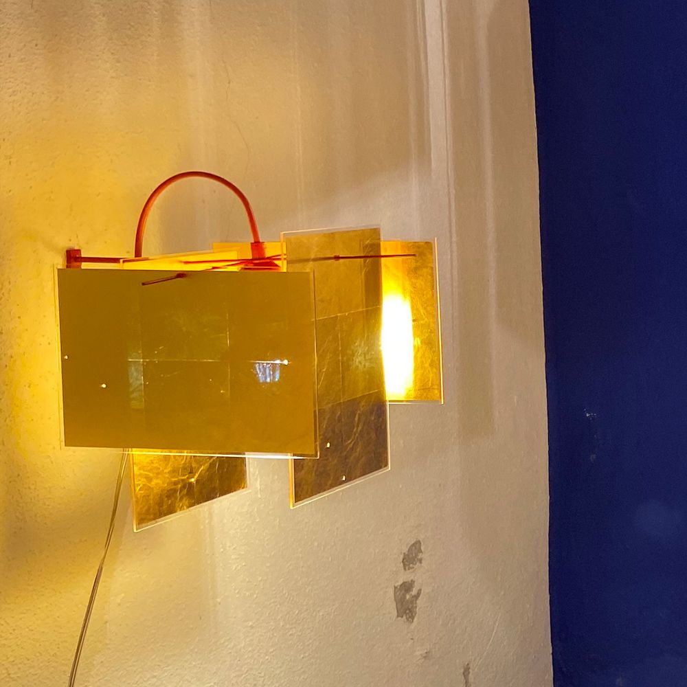 Ingo Maurer 24 Karat Blau Wandlampe mit goldenen Blenden und warmem Licht an einer Wand.
