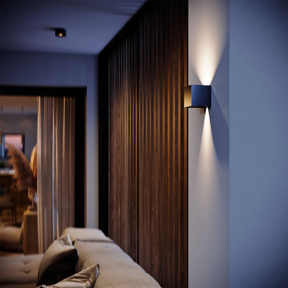 s.luce Ixa lampe murale LED avec détecteur de mouvement sur un mur moderne, accentuée par une lumière chaude.