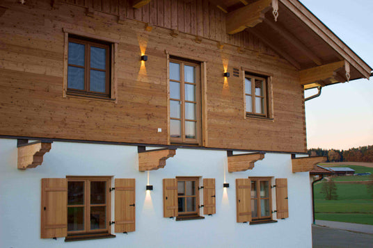 Traditionelles Holzhaus mit Fensterläden und warmem Licht in der Abenddämmerung.