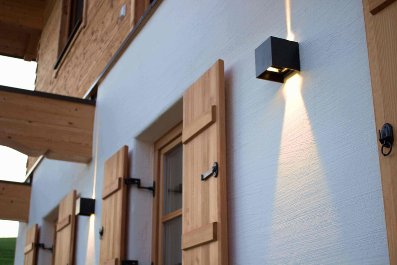 Moderne Außenbeleuchtung an Holzfassade mit Fensterläden, s.luce Lichtakzent auf Wand.