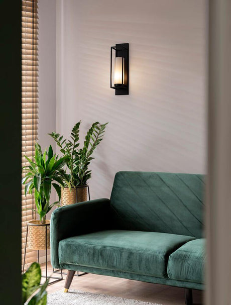 Juliet væglampe E27 på en væg over en grøn sofa med planter i baggrunden.