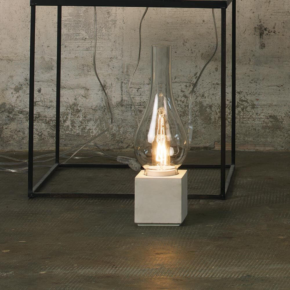 Karman Amarcord Tischlampe auf einem Tisch mit klarer Glasstruktur und Betonfuß, elegant und modern.