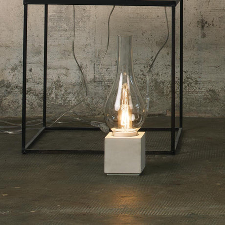 Karman Amarcord Tischlampe auf einem Tisch mit klarer Glasstruktur und Betonfuß, elegant und modern.