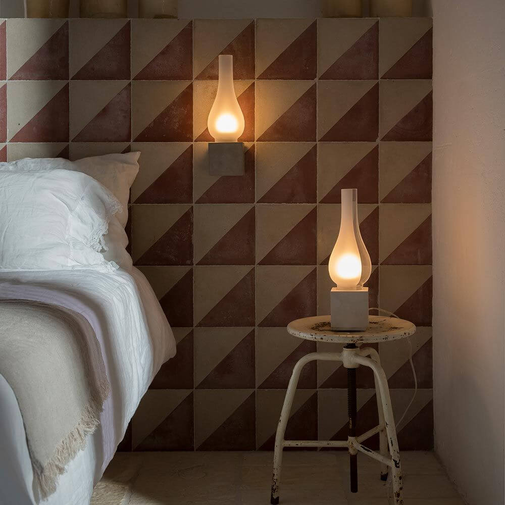 Karman Amarcord Tischlampe auf einem Tisch neben dem Bett in einem modernen Schlafzimmer mit geometrischen Wänden.