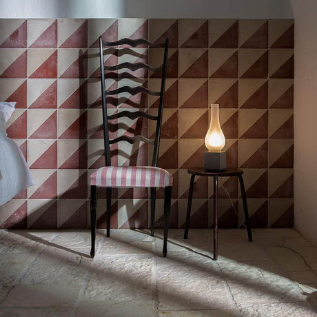 Karman Amarcord Tischlampe auf einem Tisch neben einem Stuhl vor einem geometrischen Wanddesign.