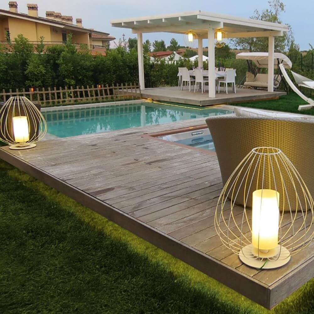 Karman Cell Outdoor-Bodenlampe IP65 auf Holzdeck neben Pool, umgeben von Rasen und Gartenmöbeln.