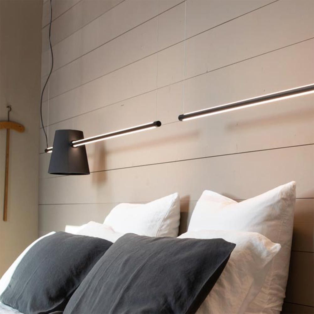 Karman Cupido LED Balkenleuchte Tunable via App über einem Bett mit weißen und grauen Kissen.