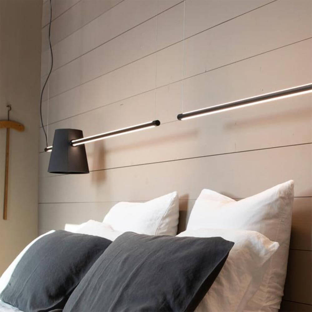 Karman Cupido Schirm für Cupido LED-Balkenlampe über einem Bett mit dekorativen Kissen.