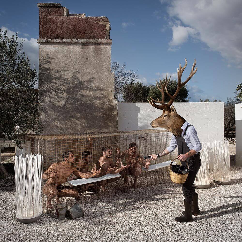 Surrealistische Szene mit einem Mann mit Geweih, der nackt sitzende Personen bedient.