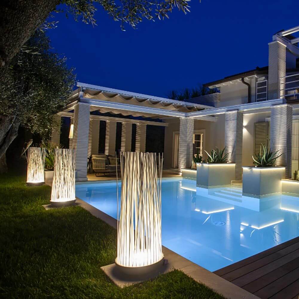 Karman Don't Touch LED Außen-Bodenleuchte in elegantem Schilfrohr-Design, beleuchtet den Garten am Pool bei Nacht.