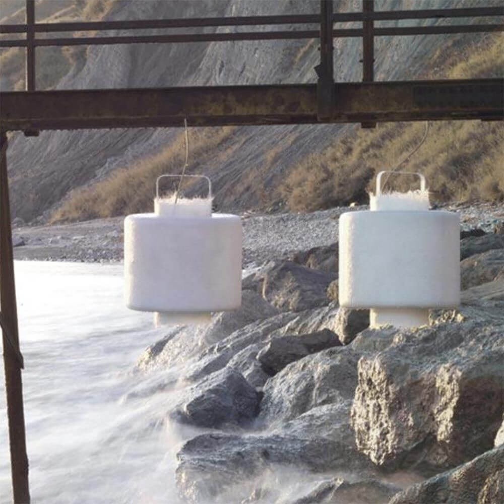 Karman Kimono LED Hängeleuchte im Freien, schwerelos über Felsen am Wasser hängend.