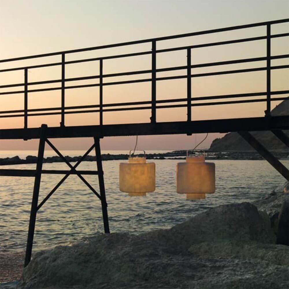 Karman Kimono LED Außen-Hängeleuchte IP65 hängen über einem Holzsteg am Wasser während des Sonnenuntergangs.
