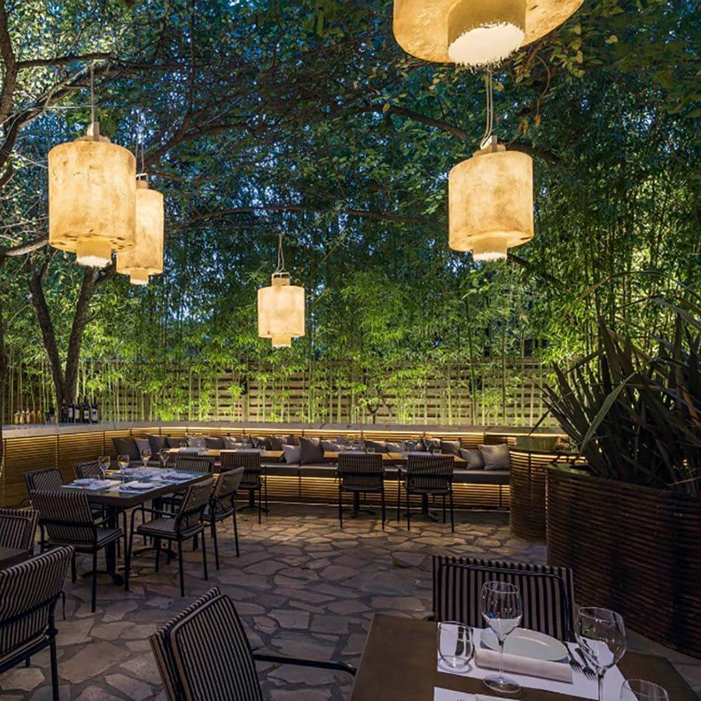 Karman Kimono LED Hängeleuchte im Außenbereich, gemütliche Terrasse mit modernen Pendelleuchten umgeben von Pflanzen.