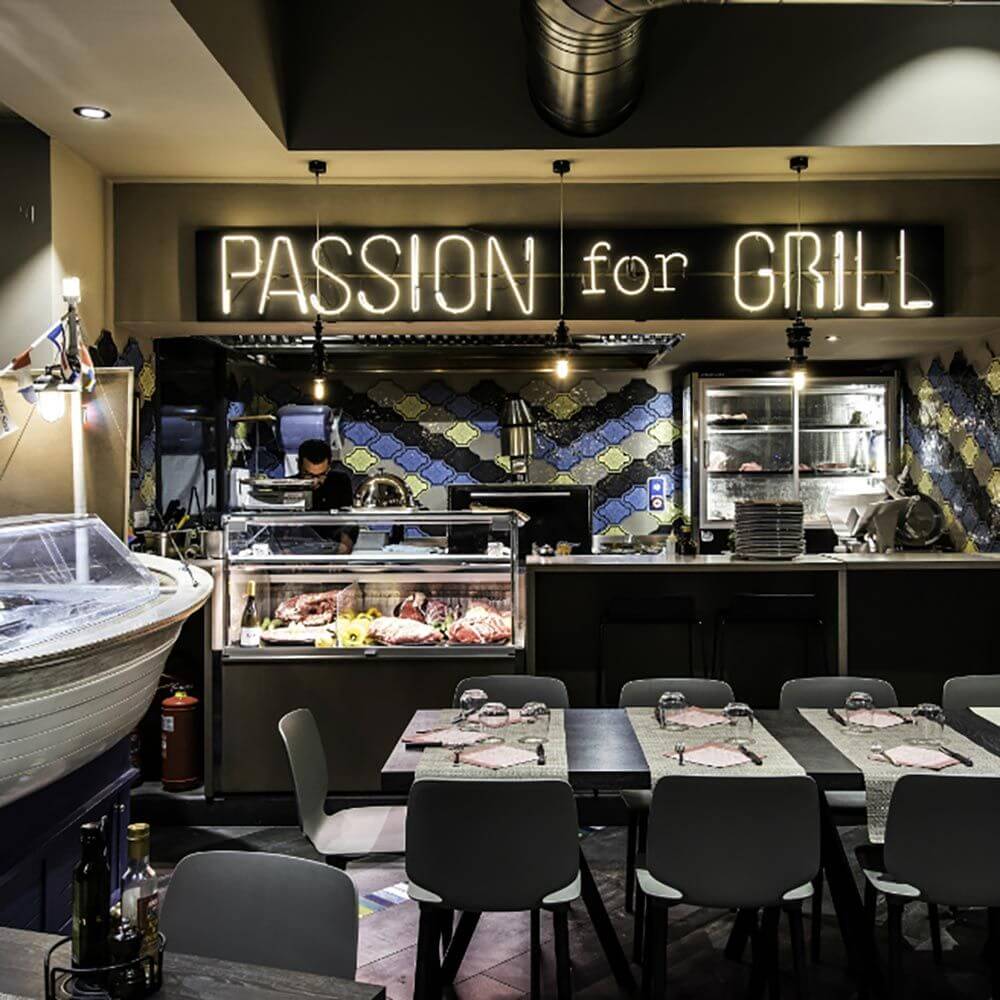 Restaurantinterieur mit dem Schriftzug "PASSION for GRILL" und offener Grillstation im Hintergrund.