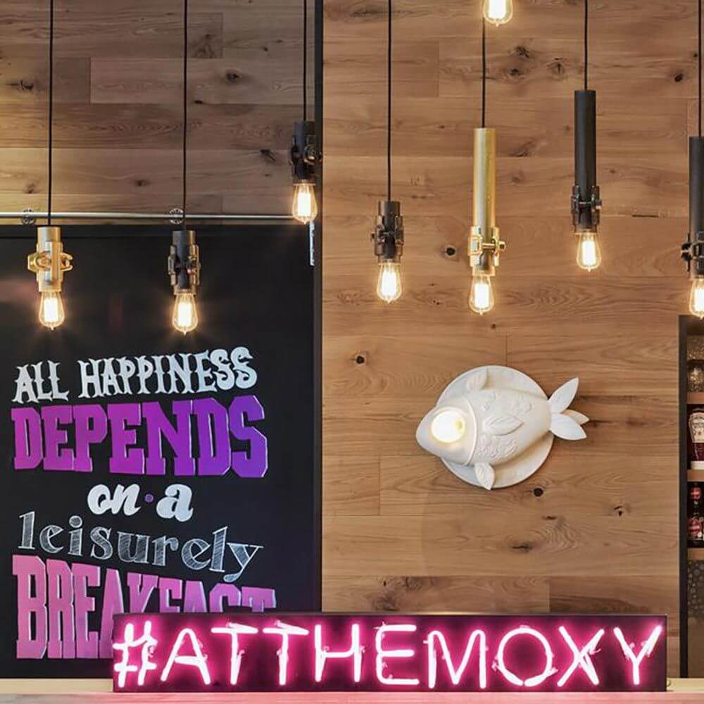 Kreative Wandlampe in Fischform im stilvollen Café mit Pendelleuchten und buntem Schriftzug #ATTHEMOXY.