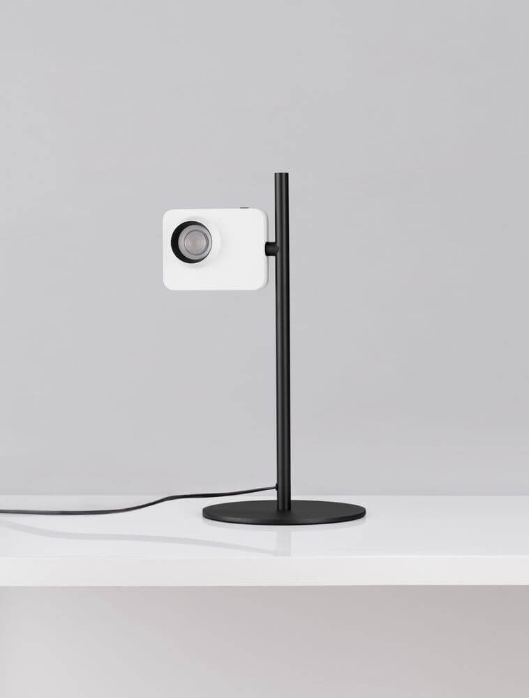 Kedros LED Tischleuchte 3000K mit Lampenfuß auf einem Tisch, moderne Designleuchte in Schwarz und Weiß.