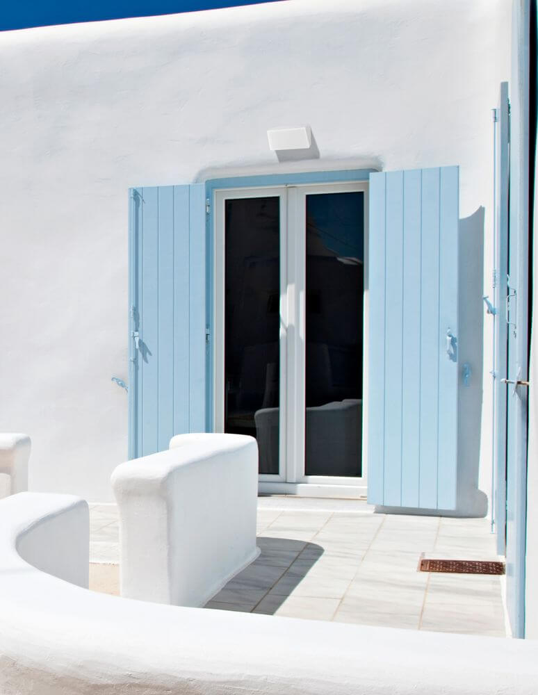 Hellblau gestrichene Fensterläden vor einer weißen Wand, mit einem modernen Balkon im mediterranen Stil.
