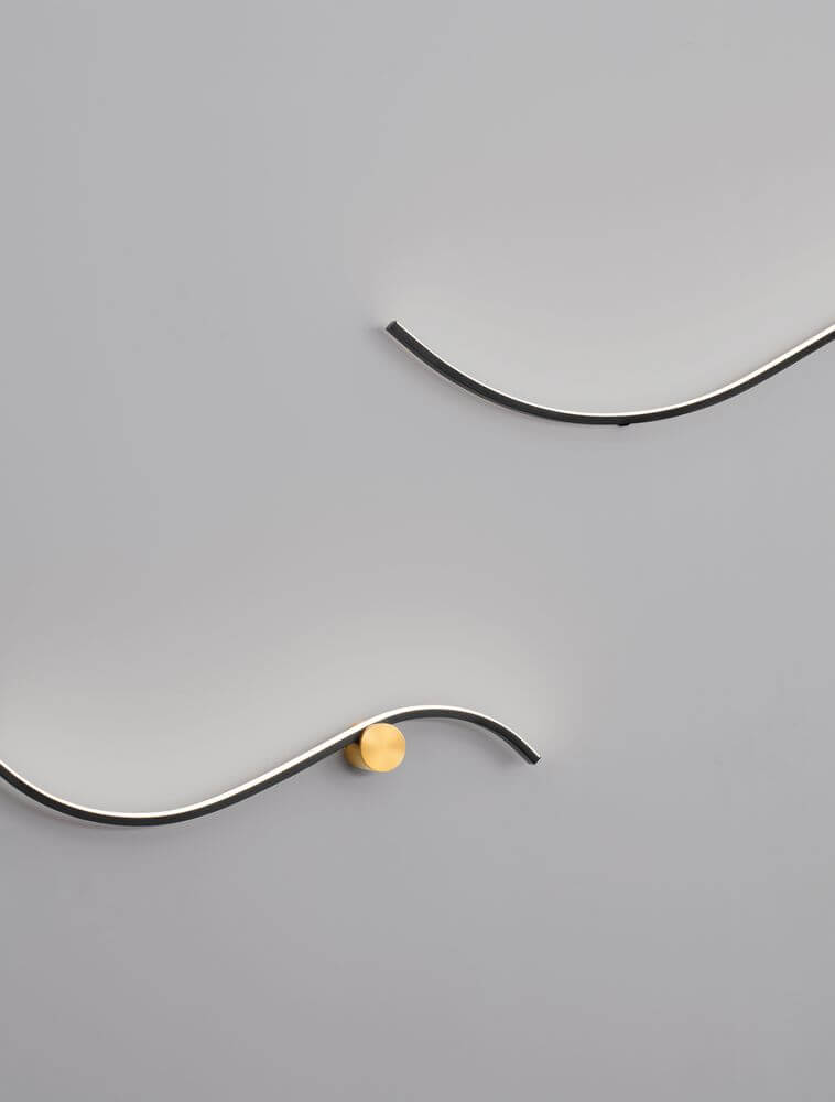 Kima LED Wandleuchte Geschwungen 3000K Schwarz, Gold an grauer Wand, stilvolles Design mit goldenen Akzenten.