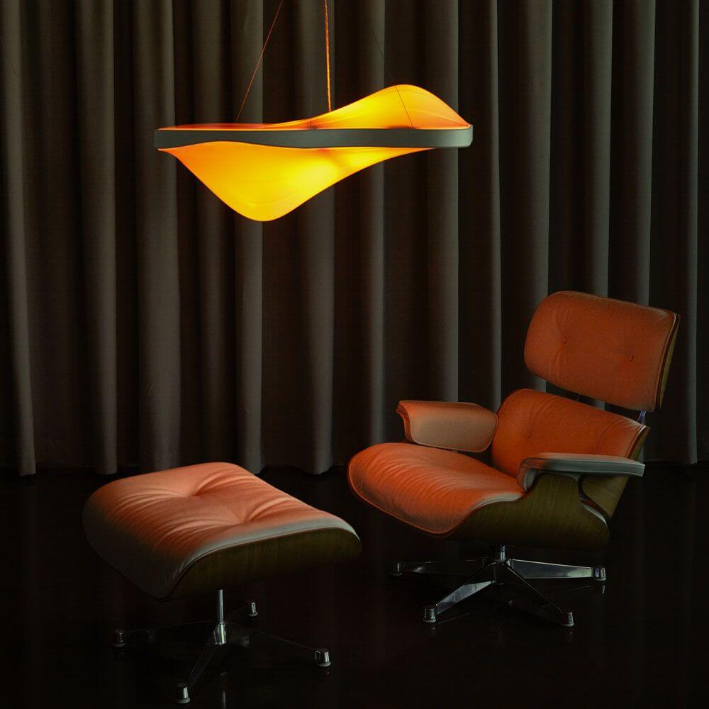 Vibe HCL Pendellampe RGBW im eleganten Innenraum mit orangefarbener Beleuchtung und modernem Sessel.