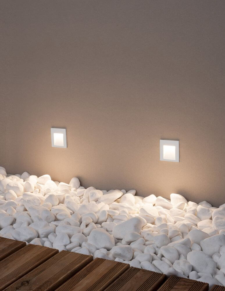 Krypton LED Außenwandeinbauleuchte quadratisch mit 3000K Weißlicht, IP54, an Wand mit Kies.