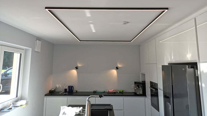 Moderne Küche mit indirekter Beleuchtung und elegantem Deckendesign, hellgrauen Wänden und hochwertigen Geräten.