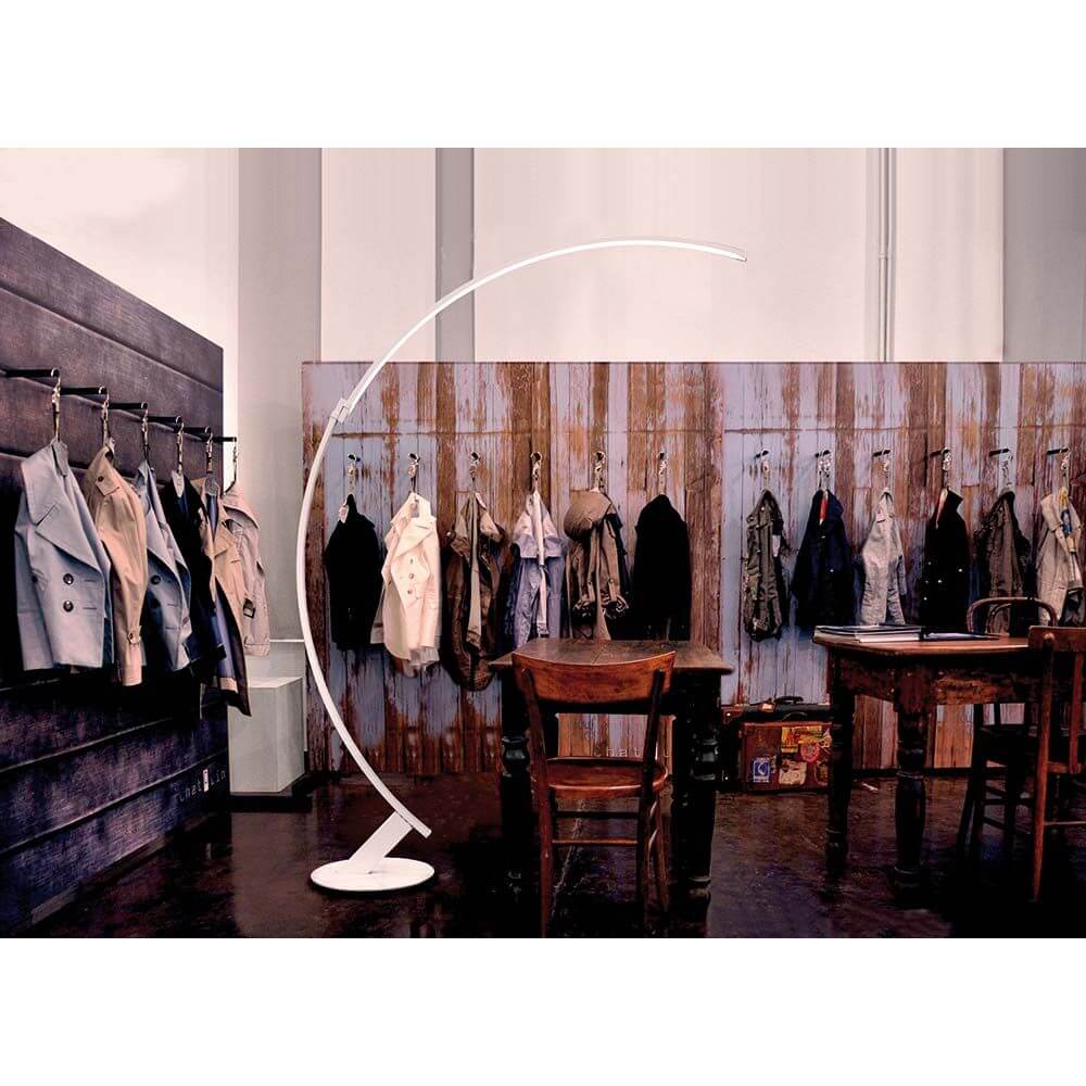 Kundalini LED Bogen-Stehlampe Kyudo Dimmbar in einem stilvollen Raum mit Kleiderständern und Holzmobiliar.