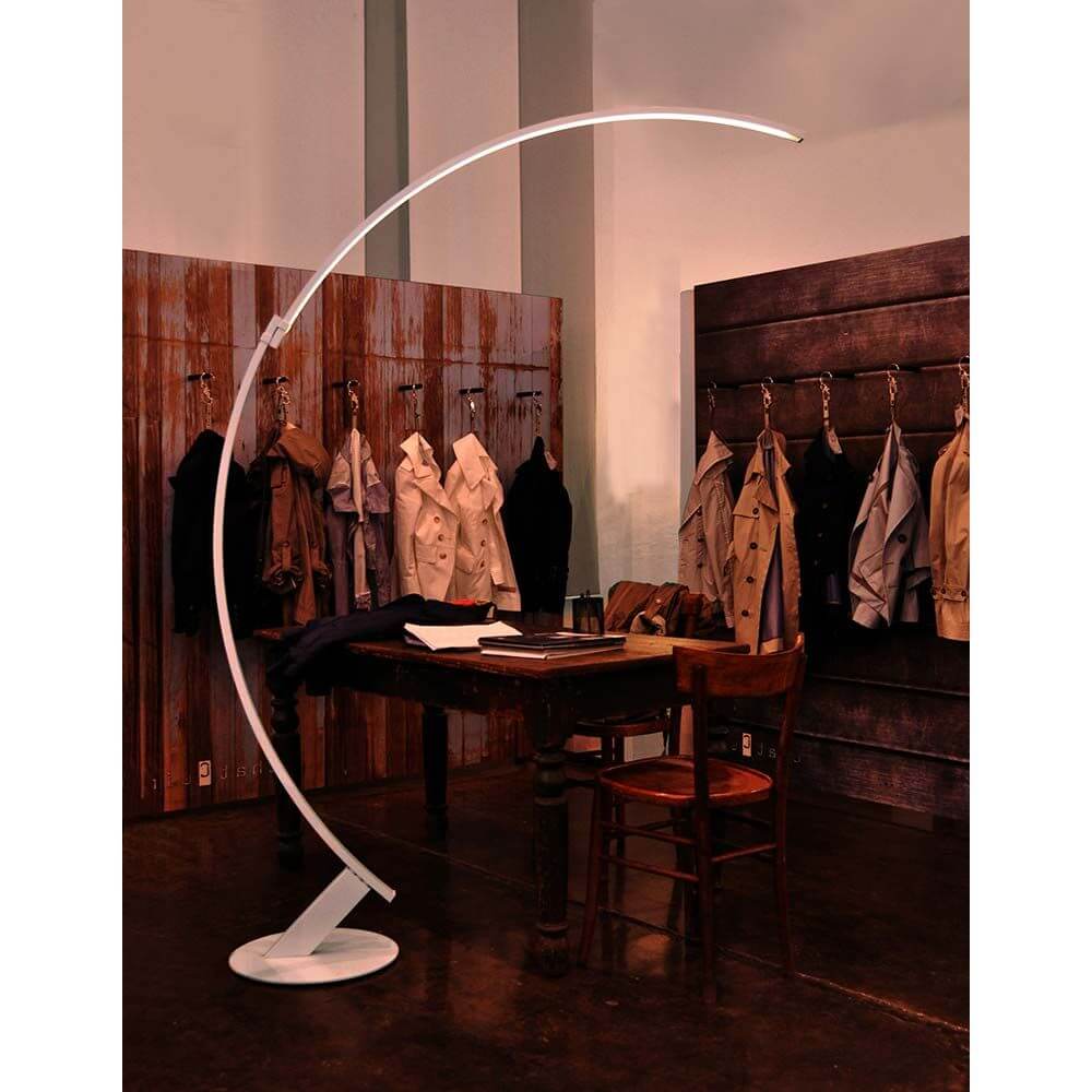 Kundalini LED Bogen-Stehlampe Kyudo Dimmbar in eleganter Umgebung mit einem Tisch und Jacken im Hintergrund.