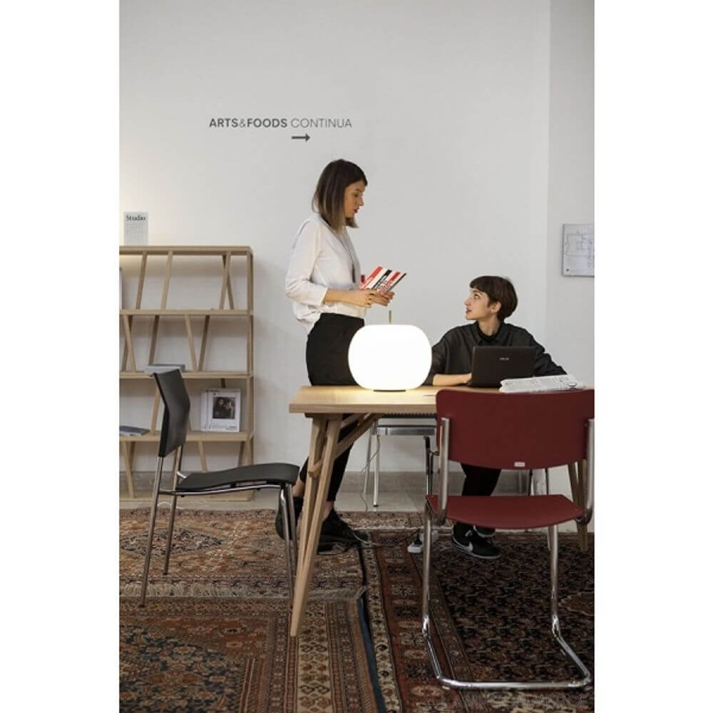 Kundalini Opalglas Tischlampe Kushi Ø33cm Dimmbar auf einem Tisch mit zwei Personen in einem modernen Raum.