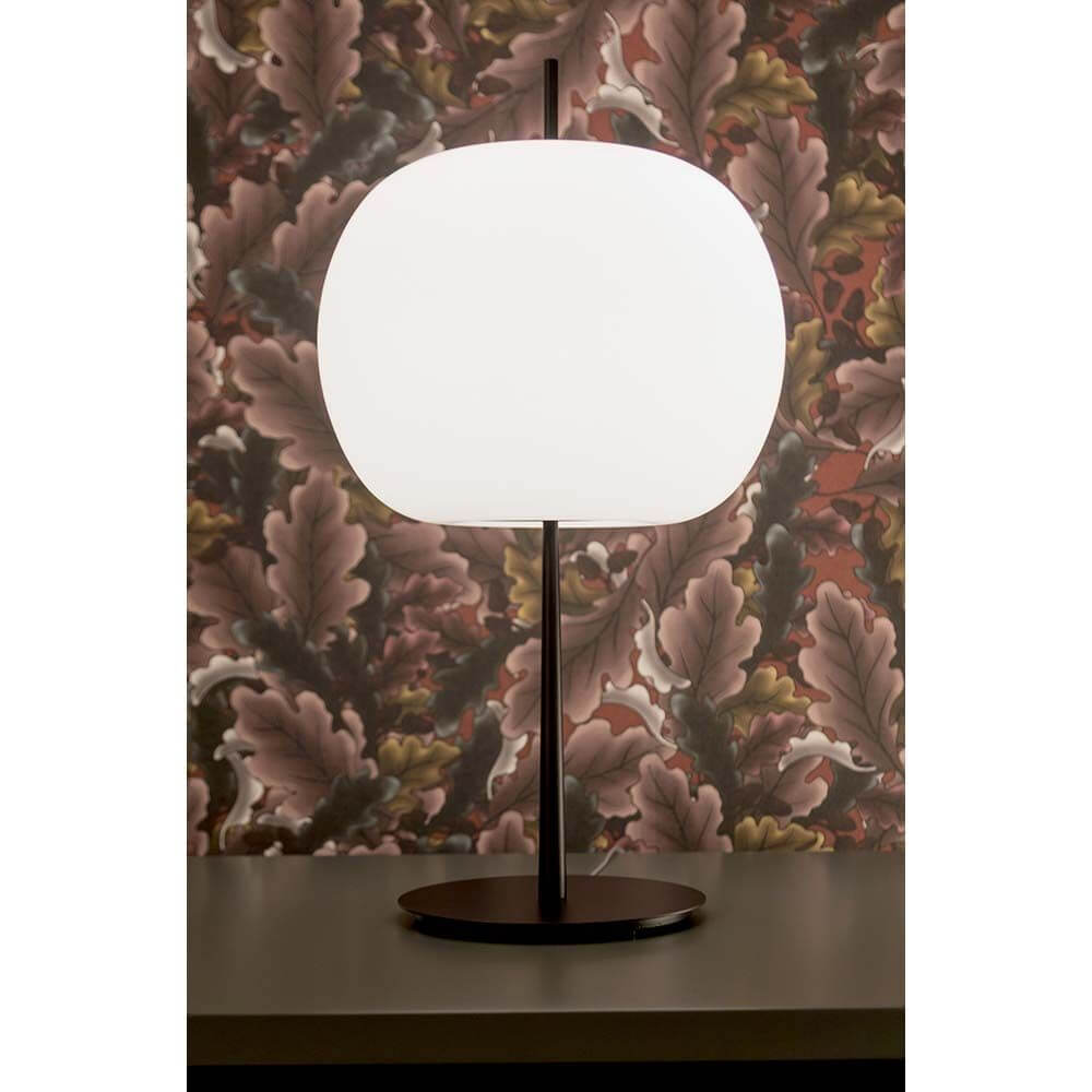 Kundalini Opalglas Tischleuchte Kushi XL 61cm mit Dimmer auf einem Tisch dekoriert vor floralem Hintergrund.