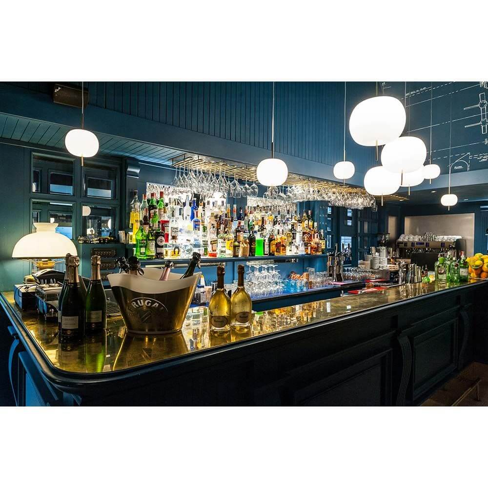 Moderne Bar mit beleuchtetem Tresen, Spirituosenregal und stilvollen Lampen im Hintergrund.